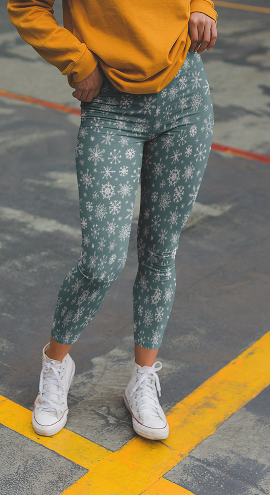 A pair of high waisted custom women's leggings that are a light blue in color and have white snowflakes all over the pants, perfect for Christmas.