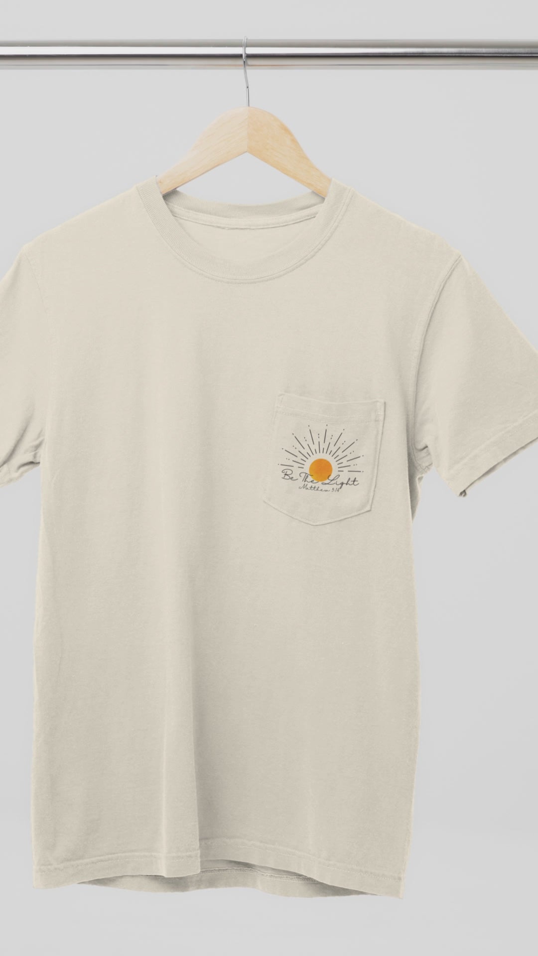 A custom Christian unisex pocket t-shirt, on the pocket that is over the left chest of the shirt is a large sun with the words Be The Light Matthew 5:14 of the Bible.