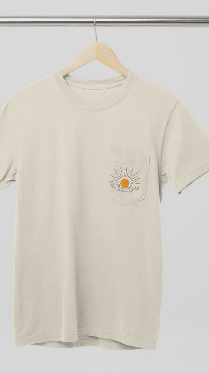 A custom Christian unisex pocket t-shirt, on the pocket that is over the left chest of the shirt is a large sun with the words Be The Light Matthew 5:14 of the Bible.