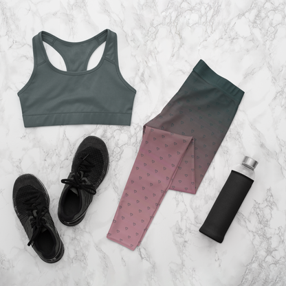 A pair of women's custom high waisted leggings that start as black at the top then fade to a light pink at the bottom, there are hearts all over the leggings then they fade into the black at the top of the pant.