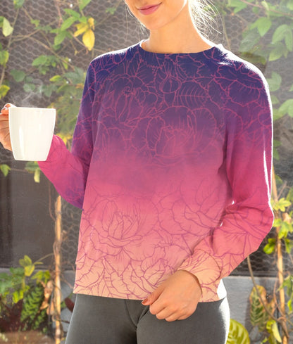 The sweater has a washed ombre pattern starting as a dark purple at the top of the neckline then fading to a light purple then to a bright pink then to a blush pink at the bottom, there is a purple floral pattern imposed on the top of the sweater.