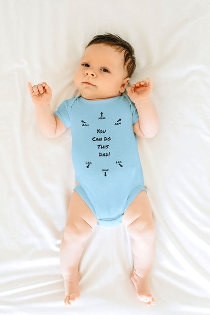 on the front of this custom infant onesie specifically meant for dads, are the words You can do this dad with arrows pointing where each leg and each arm goes along with were the babies head goes and where to close the snaps, a perfect diagram for a new father on how to put a onesie on a baby.
