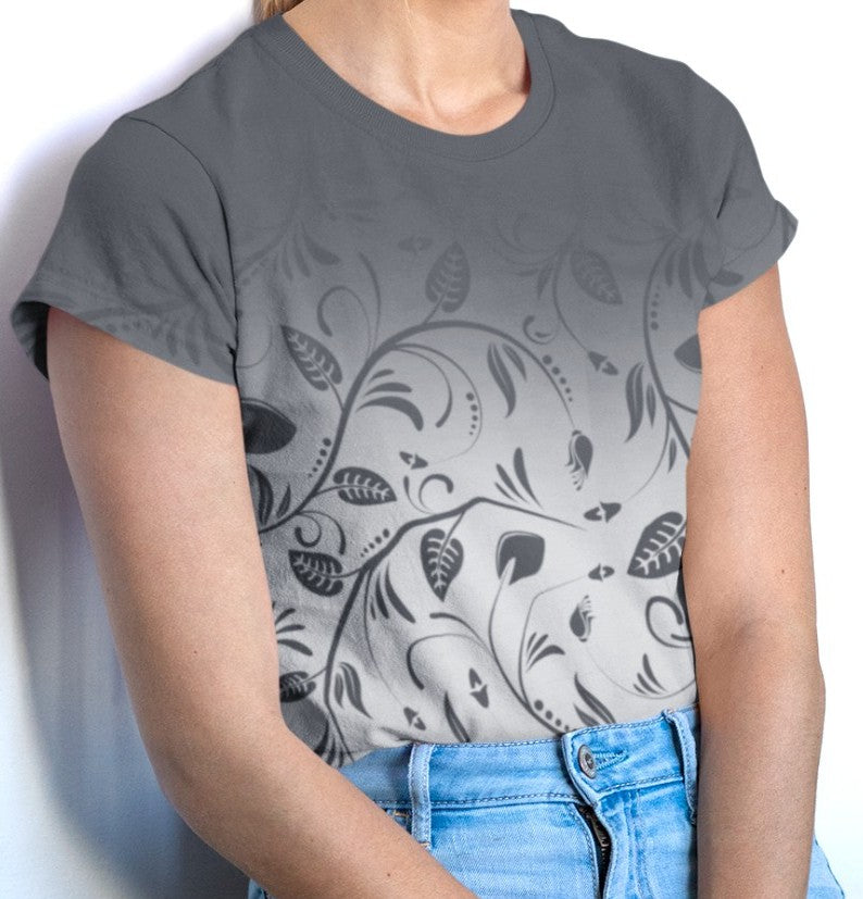 This custom women's handmade tee has a ombre pattern with the top of the shirt being a slate grey color then fading to a light grey at the waistline, there is a floral design with leaves and vines overlayed over the ombre pattern, the leaves are the same color as the dark slate color at the top of the shirt.