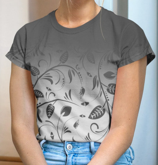 This custom women's handmade tee has a ombre pattern with the top of the shirt being a slate grey color then fading to a light grey at the waistline, there is a floral design with leaves and vines overlayed over the ombre pattern, the leaves are the same color as the dark slate color at the top of the shirt.