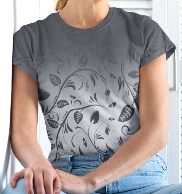 This custom women's handmade tee has a ombre pattern with the top of the shirt being a slate grey color then fading to a light grey at the waistline, there is a floral design with leaves and vines overlayed over the ombre pattern, the leaves are the same color as the dark slate color at the top of the shirt.